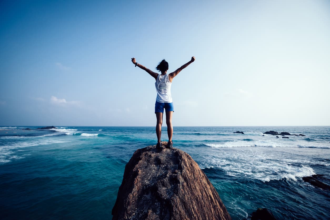 Women stood on rock over looking ocean with hands in the air