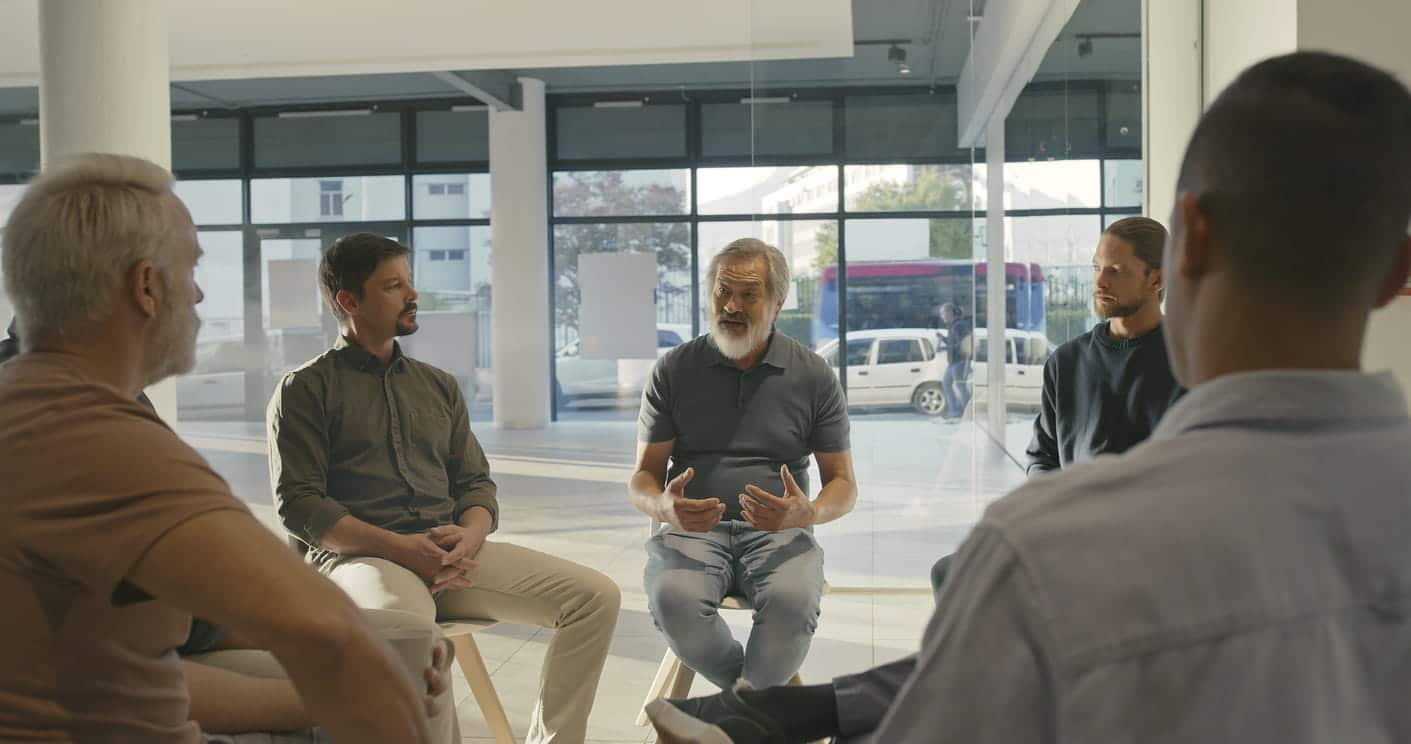 Men sat in circle with one gesturing as he's talking